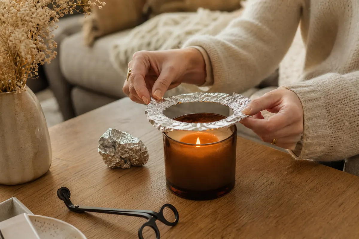 Bougie en pot avec un tunnel de cire, papier aluminium et coupe-mèche posés sur une table basse en bois