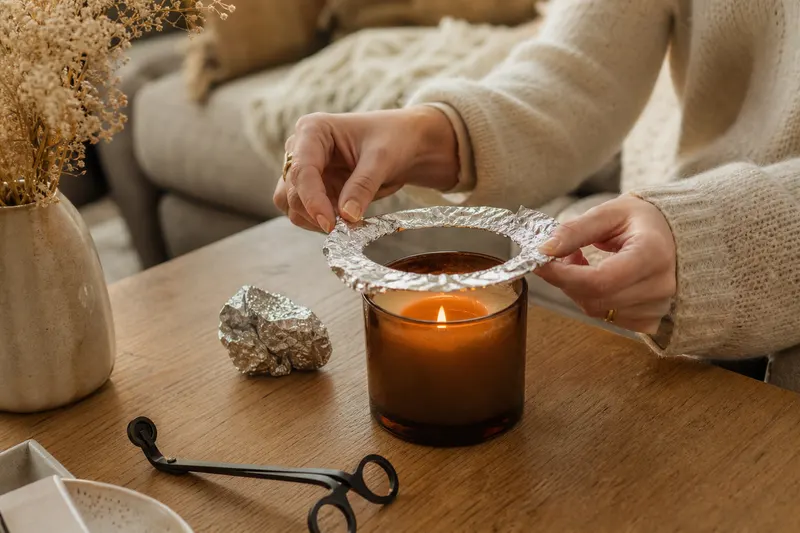 Bougie en pot avec un tunnel de cire, papier aluminium et coupe-mèche posés sur une table basse en bois