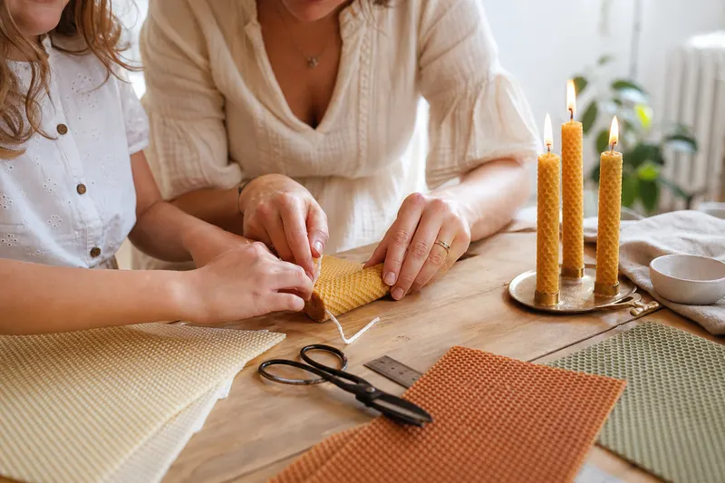 Mains d'une adulte et d'un enfant roulant une feuille de cire d'abeille gaufrée autour d'une mèche sur une table en bois