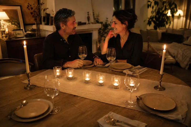 Table de dîner éclairée par un chemin de photophores et deux chandeliers en laiton avec des chandelles ivoire