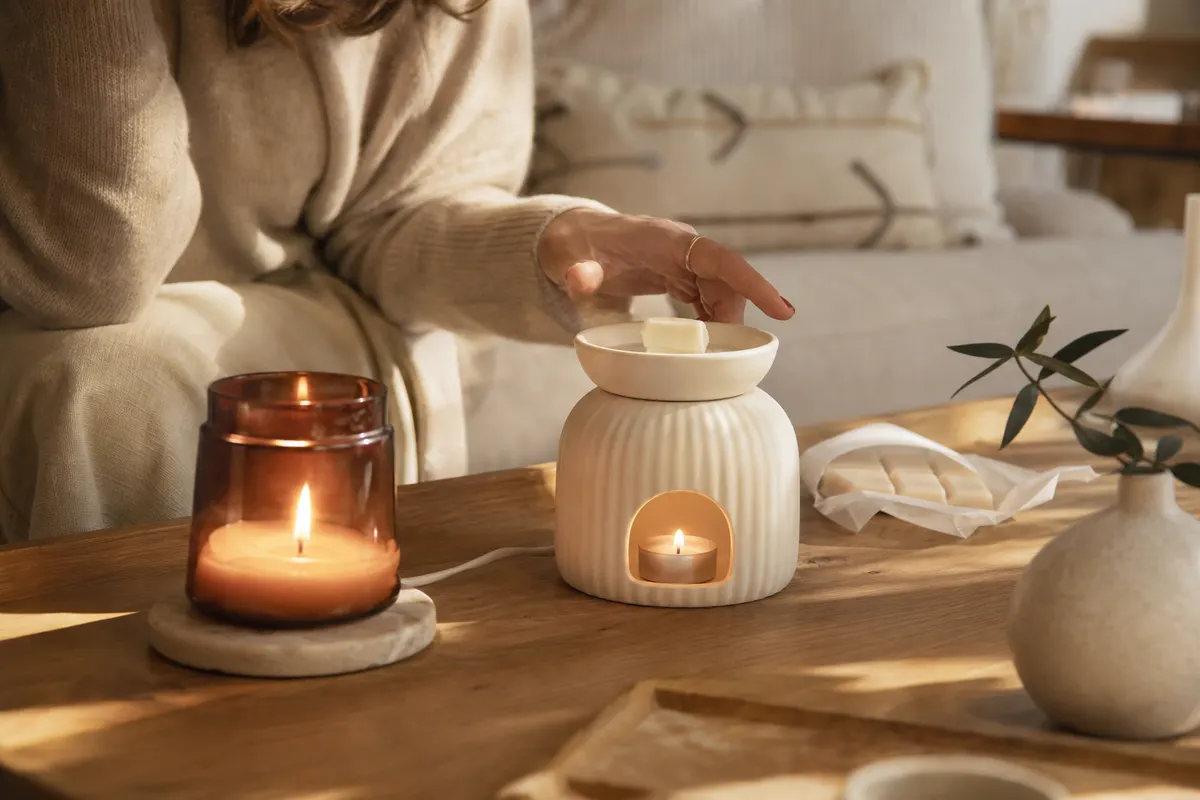 Bougie parfumée allumée et brûle-parfum électrique avec un fondant, côte à côte sur une table basse