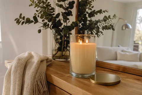 Grande bougie parfumée d'hiver allumée dans un pot en verre, couvercle posé à côté, sur une console en bois clair