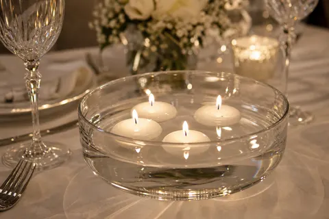 Bougies flottantes blanches allumées dans une coupe en verre sur une table de restaurant nappée de blanc