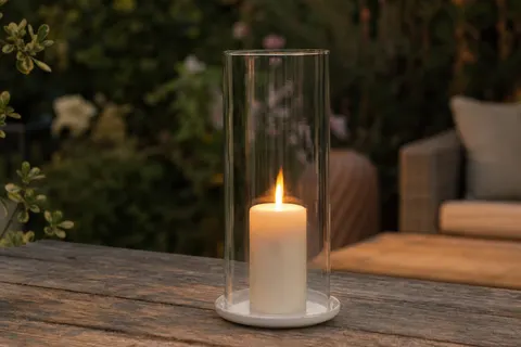Haut cylindre de verre transparent posé sur une bougie pilier allumée, sur une table de jardin en bois au crépuscule