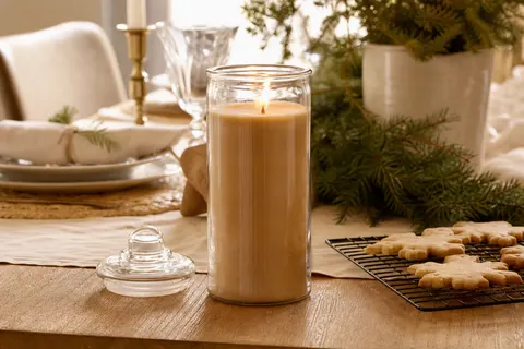 Bougie en jarre de verre allumée sur une table en chêne avec des sablés et une branche de sapin