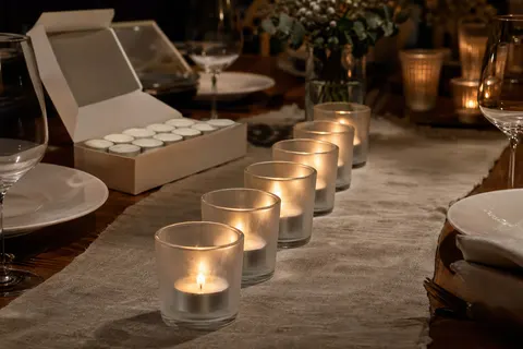 Bougies chauffe-plat blanches allumées dans des photophores en verre au centre d'une table dressée