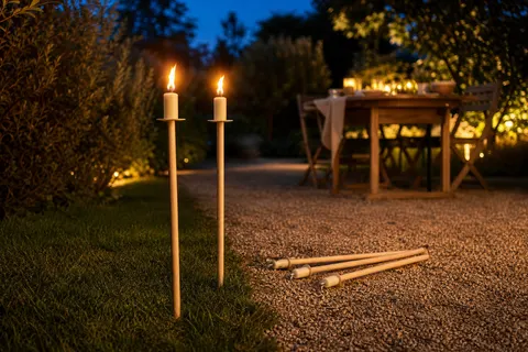 Torches de jardin en cire à manche de bois plantées dans une pelouse au crépuscule, flammes allumées