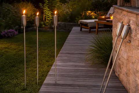 Torches de jardin en acier inoxydable allumées le long d'une terrasse en bois au crépuscule