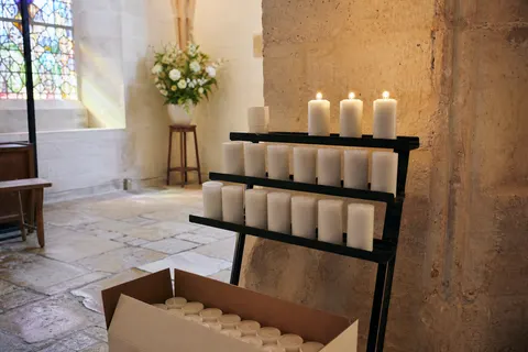 Veilleuses blanches de neuvaine sur un présentoir métallique dans une chapelle en pierre claire