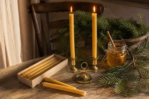 Bougies fines en cire d'abeille couleur miel dans leur boîte et dans un chandelier en laiton