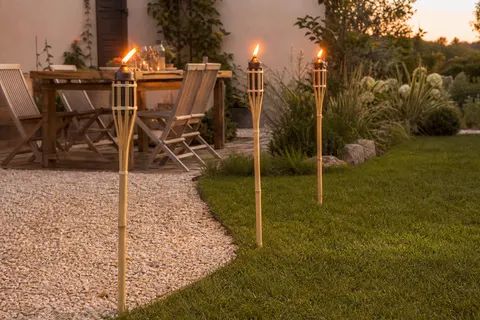 Torches de jardin en bambou allumées plantées le long d'une allée gravillonnée au crépuscule