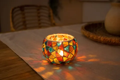 Bougeoir en verre mosaïque coloré avec bougie chauffe-plat allumée posé sur une table en bois et un chemin de table en lin