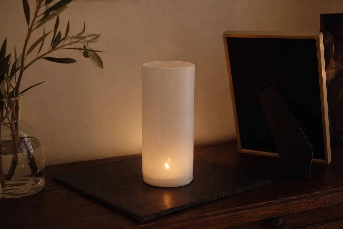 Veilleuse blanche unie allumée sur une plaque d'ardoise, posée sur une commode en bois sombre