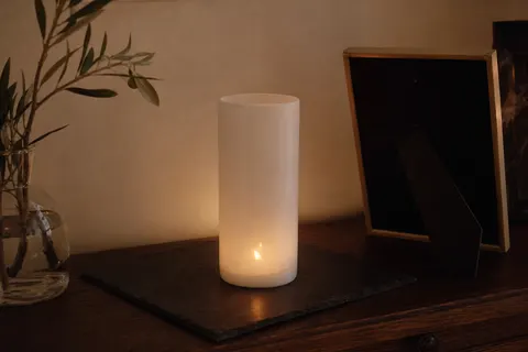 Veilleuse blanche unie allumée sur une plaque d'ardoise, posée sur une commode en bois sombre