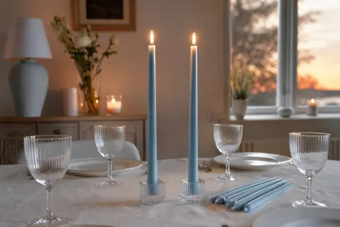 Longues bougies de table bleu arctique dans des bougeoirs en verre sur une nappe en lin blanc