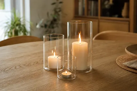 Trois photophores cylindriques en verre de hauteurs différentes avec bougies allumées, groupés sur une table en chêne