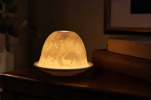 Dôme photophore en porcelaine blanche éclairé par une bougie, révélant son motif gravé, posé sur une commode en bois
