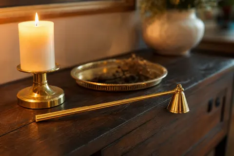Éteignoir doré à long manche posé sur une console près d'un bougeoir en laiton et d'une chandelle allumée