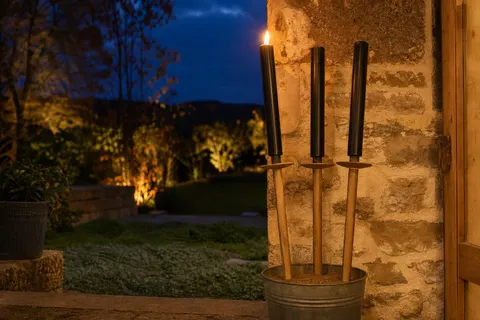 Torches en cire à manche de bois et collerette, dont une allumée, plantées dans un seau de sable