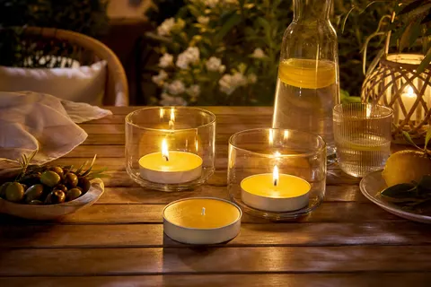 Chauffe-plats jaunes à la citronnelle allumés dans des photophores en verre sur une table de jardin