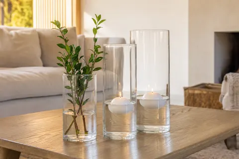 Trois cylindres en verre de hauteurs différentes avec bougies flottantes allumées sur une table basse