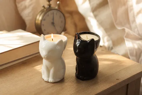 Deux bougies parfumées en pots de dolomite en forme de chat, blanc et noir, sur une table de chevet en bois