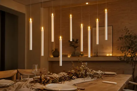 Bougies coniques LED suspendues à des fils fins au dessus d'une table en bois dressée pour un dîner