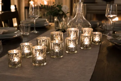 Douze photophores en verre mercurisé argent avec bougies chauffe-plat allumées sur une table