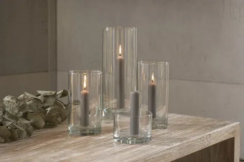 Quatre chandelles courtes gris clair de 11 cm dans des photophores en verre sur une console
