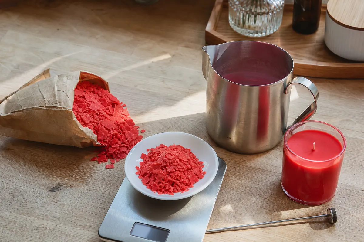 Flocons de colorant rouge pour bougies dans une coupelle sur une balance, avec pichet de coulée en inox
