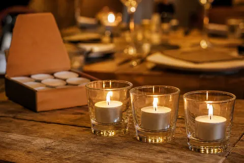 Bougies chauffe-plat hautes en godet aluminium allumées dans des verres photophores sur une table de restaurant