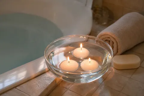 Trois bougies flottantes blanches allumées dans une coupe en verre sur le rebord d'une baignoire