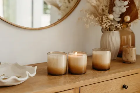 Trois petites bougies parfumées en pot de verre dégradé sur une console d'entrée, une flamme allumée