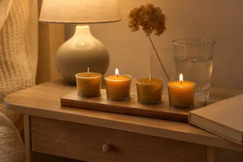 Quatre bougies votives en cire d'abeille dans leurs godets sur un plateau en bois, deux flammes allumées