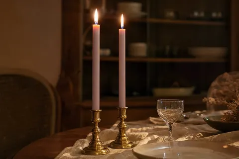Deux chandelles rose antique allumées dans des bougeoirs en laiton sur une table en bois