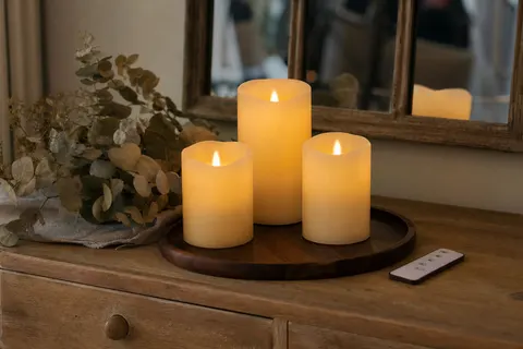 Trois bougies piliers LED ivoire allumées sur un plateau en bois avec leur télécommande