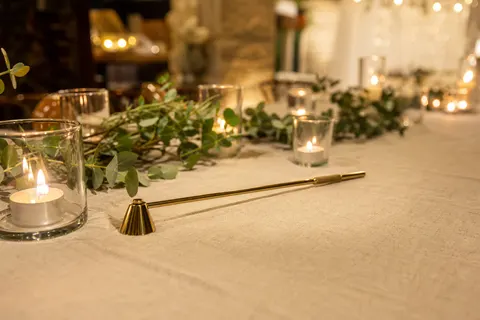 Éteignoir doré à manche de 25 cm posé sur une table de réception entourée de photophores allumés