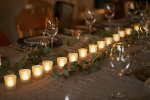 Photophores en verre dépoli alignés sur une table de fête, éclairés par des bougies chauffe-plat électriques à lueur chaude.