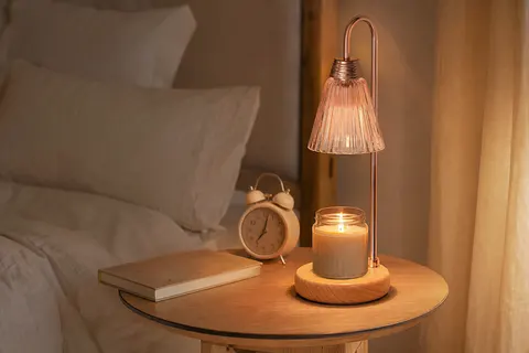 Lampe chauffe-bougie rose sur une table de chevet éclairant une bougie en pot dans une chambre