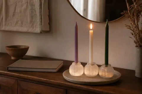 Bougies fines colorées dans des bougeoirs en sélénite translucide posés sur une commode en bois