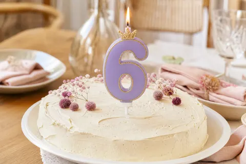 Bougie chiffre 6 lilas à couronne dorée allumée sur un gâteau nappé de crème ivoire