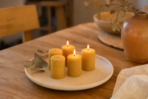Cinq petites bougies piliers en cire d'abeille roulée au relief nid d'abeille sur une assiette en céramique