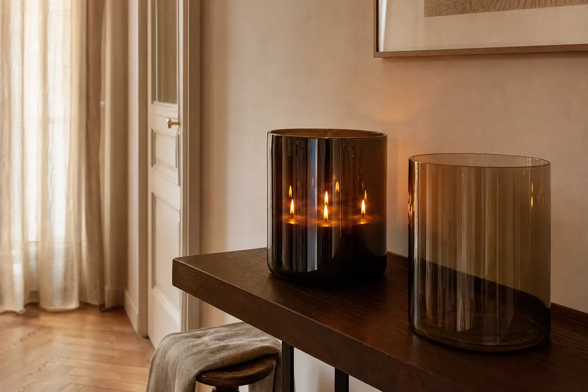Grande bougie parfumée à plusieurs mèches dans un verre soufflé sombre, allumée sur une console en bois dans une entrée